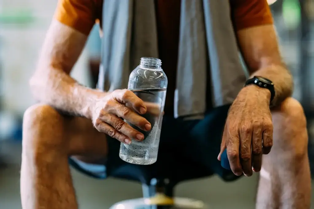 Man sitting in gym holding a water bottle after workout