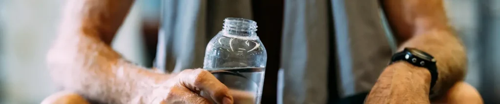 Man sitting in gym holding a water bottle after workout