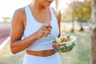 Fit woman eating a fresh heart healthy salad outdoors