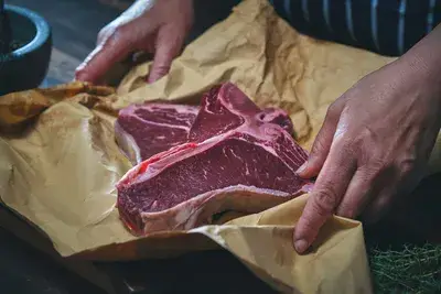 Person holding a raw T-bone steak on brown butcher paper